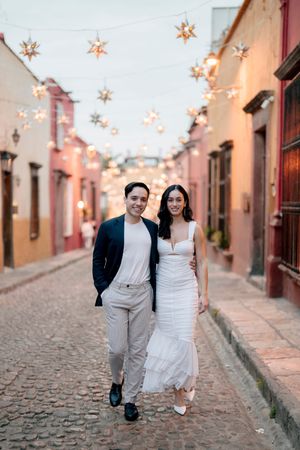 A couple strolls along a charming cobblestone street decorated with hanging star lights in Mexico.