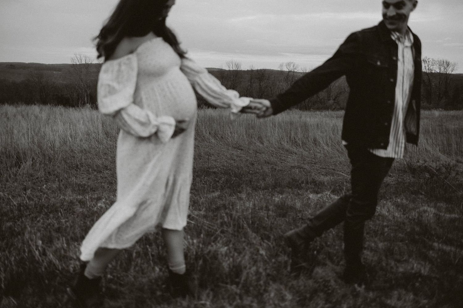 A black and white photo shows two people holding hands while walking in a grassy field in tewksbury nj.