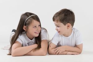 Two children lying on white floor looking at each other.