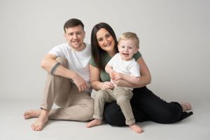 Casual family portrait with three members sitting on studio floor.