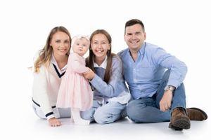 Family of four sitting together on white studio floor.
