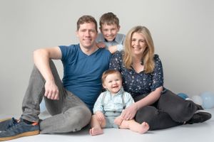 Family portrait with parents and two children sitting on grey studio floor.