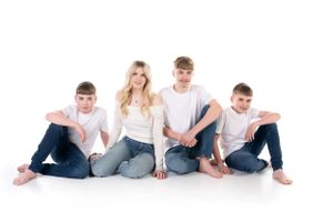 Casual family portrait with people sitting together on white background wearing jeans and neutral colors.
