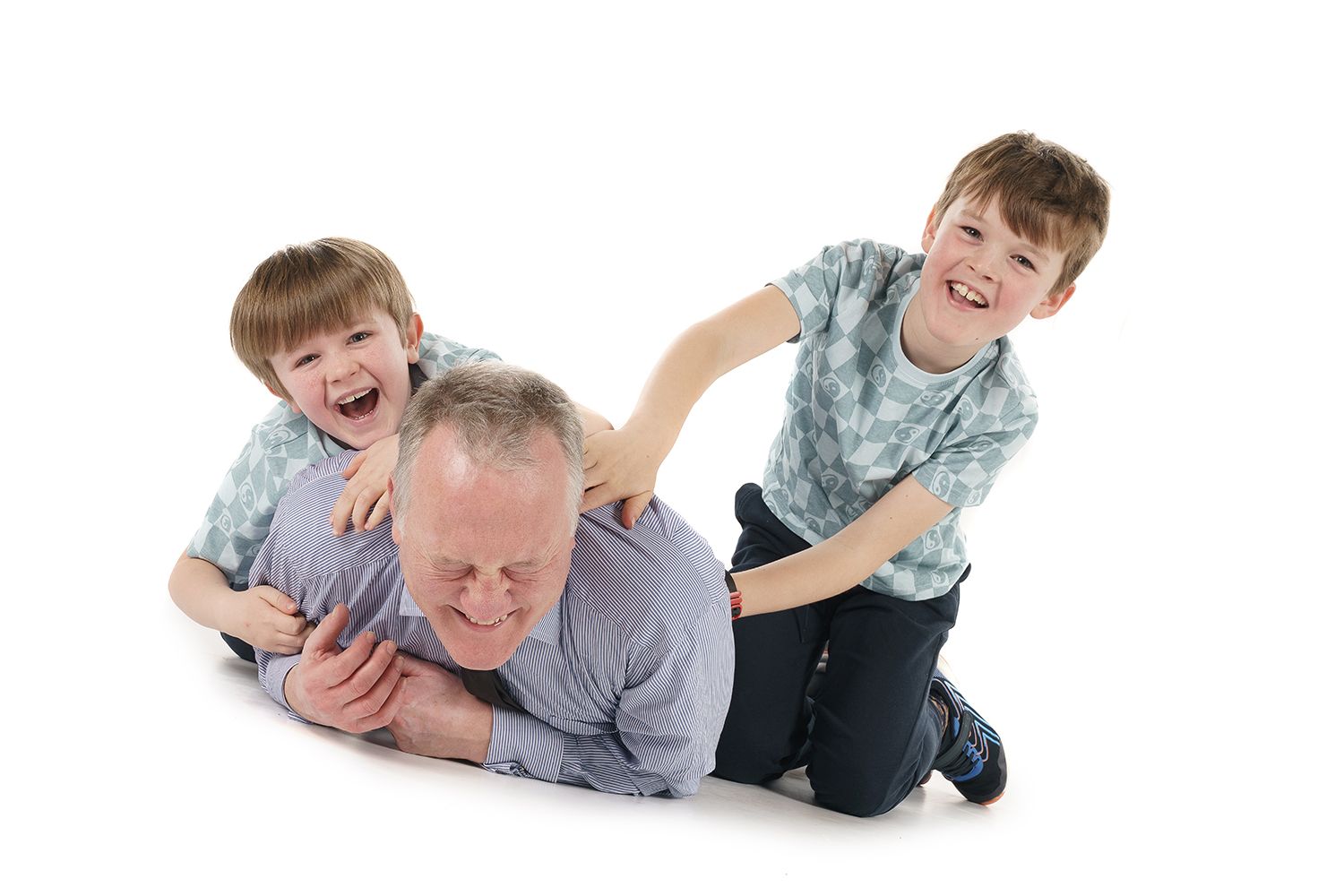Playful scene with parent and children laughing while wrestling on white background.