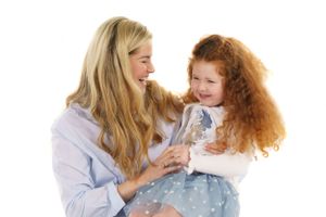 Tender moment between parent and child with curly red hair in light colored clothing.