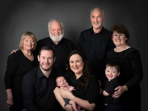 A multi-generational family portrait with members wearing black clothing against a dark background.