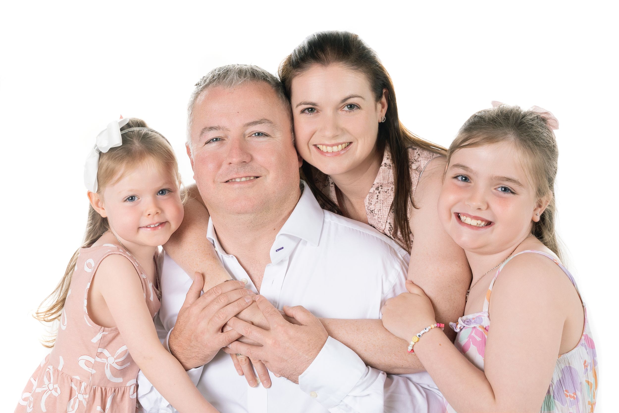 Studio family portrait with everyone wearing light colored outfits against white background.