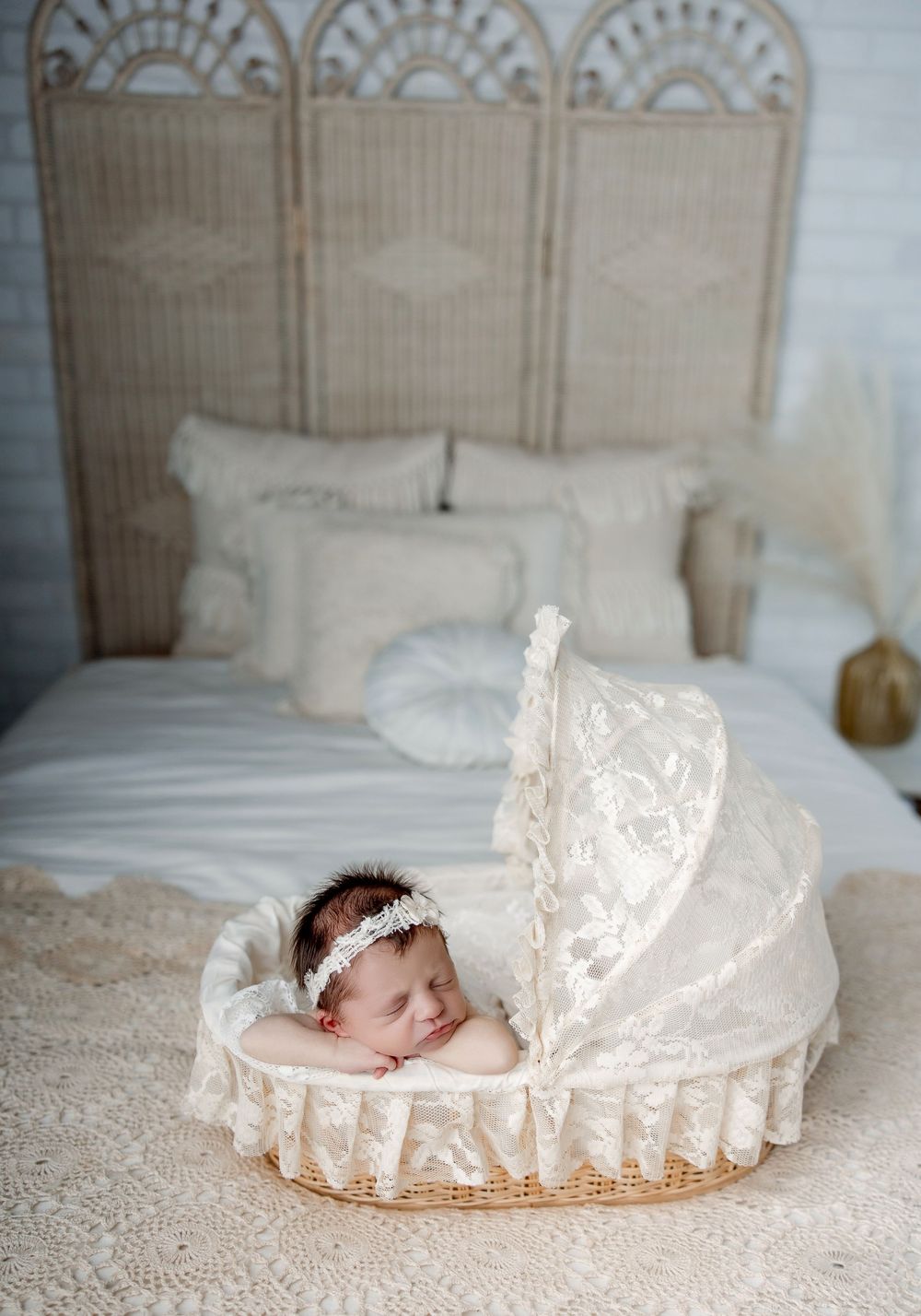 A sleeping infant wearing a lace headband lies peacefully in an antique-style basket against a creamy backdrop.