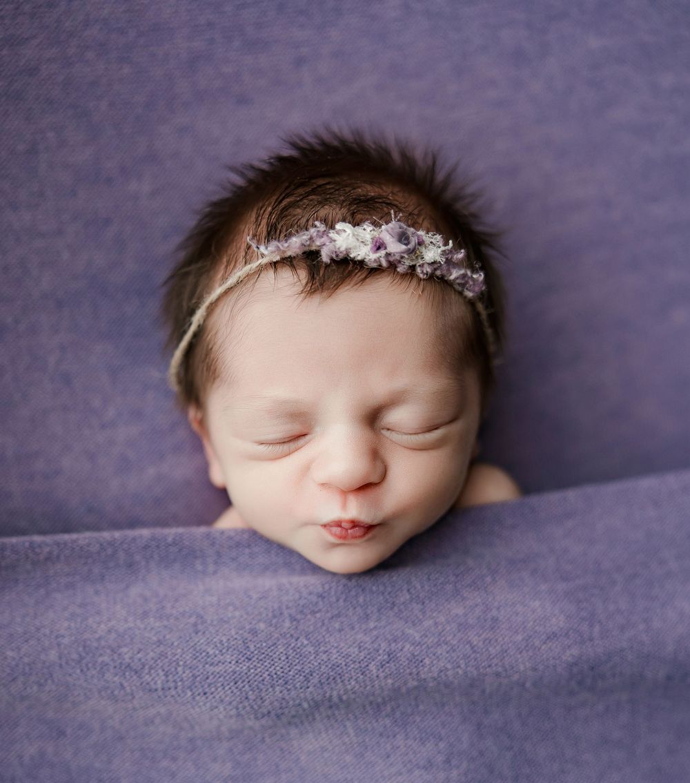 A sleeping newborn photographed in profile on purple textured fabric in fading light.