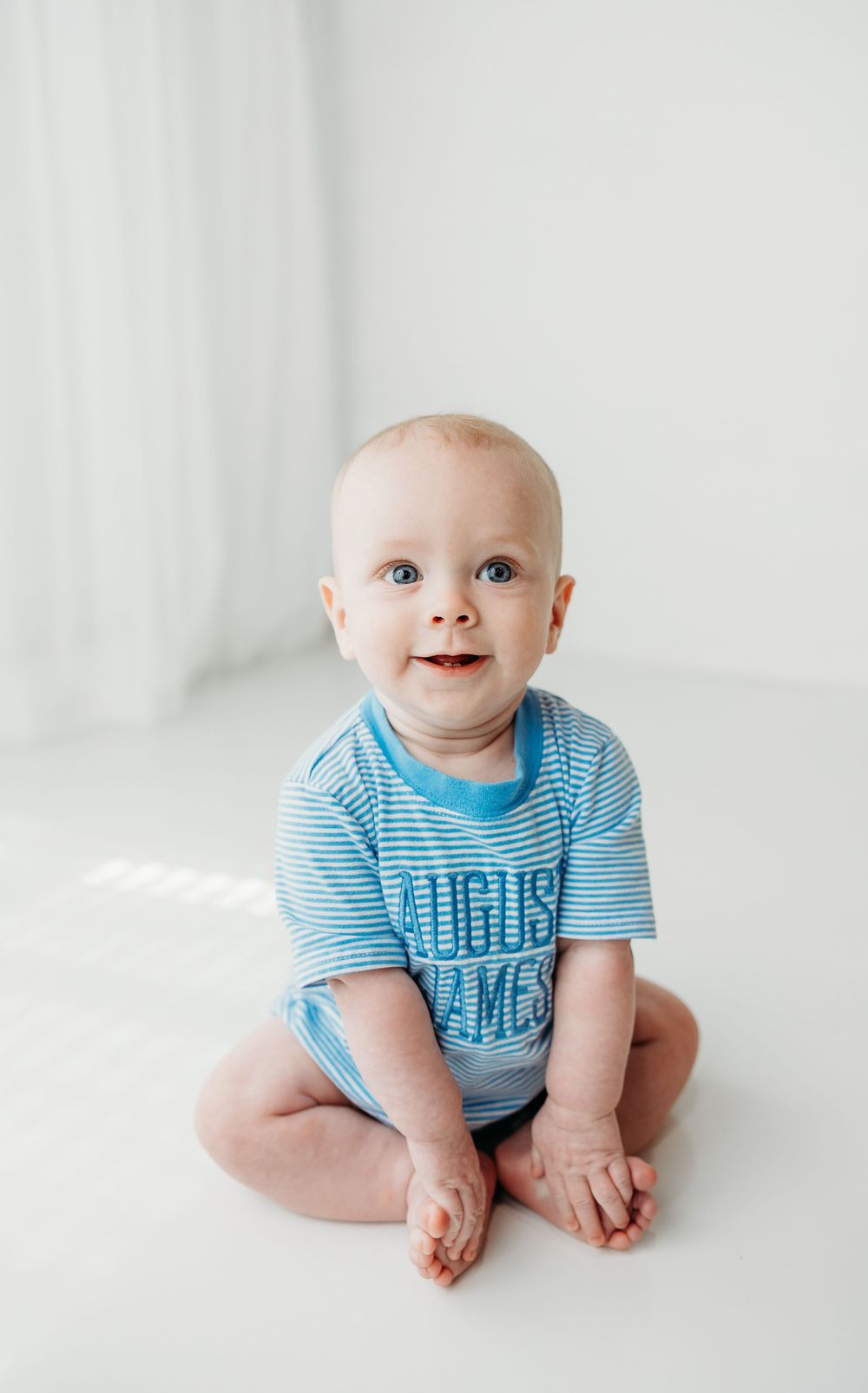 Happy baby in blue striped onesie sits and smiles on white background across four milestone photos.