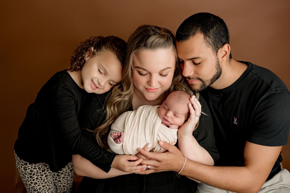 Intimate family portrait showing tender moment with newborn on brown background.