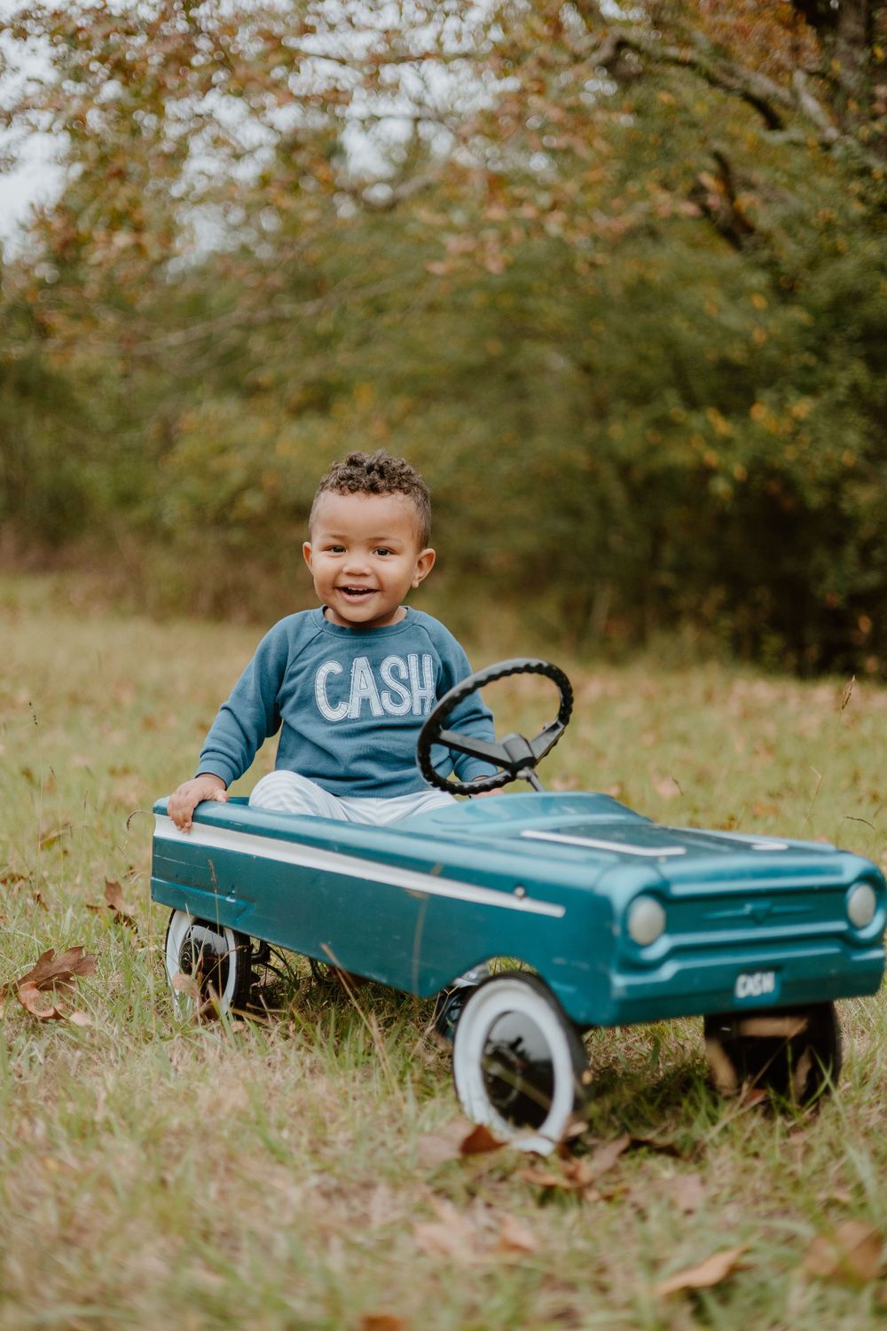 A joyful scene with a vintage-style pedal car in teal being enjoyed outdoors during autumn.