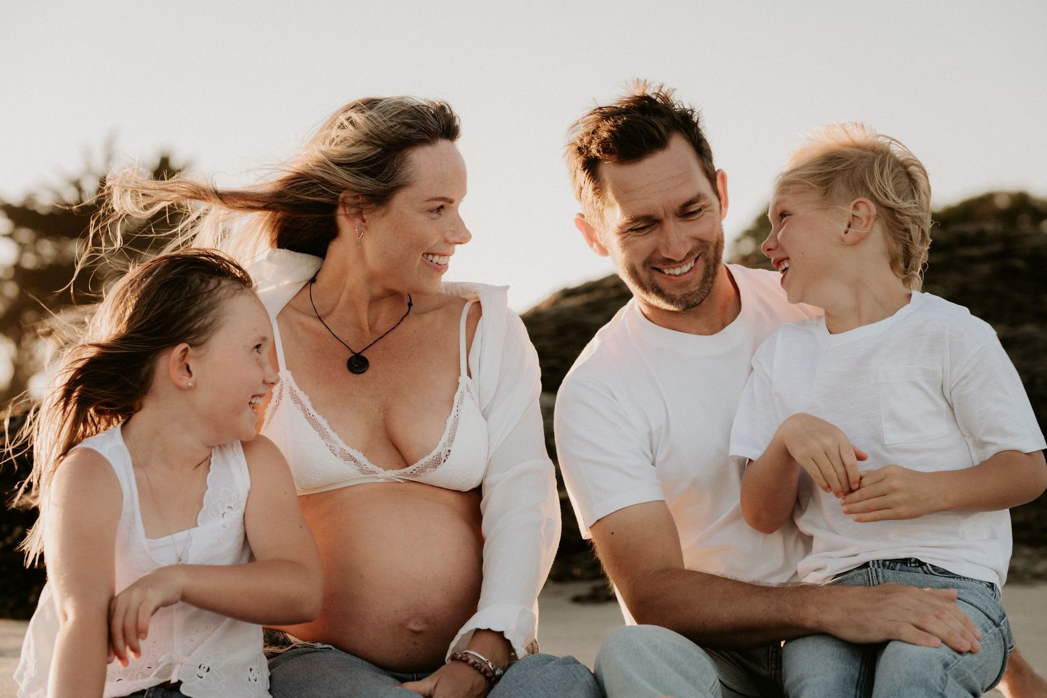 Loving parents gaze adoringly at their newborn baby wrapped in a cozy blanket against a beige backdrop with pampas grass.