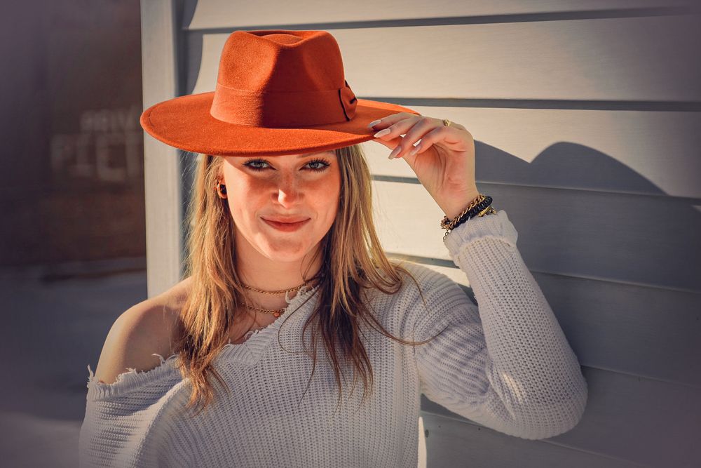 A person in a gray sweater and orange hat poses against a dark background in a series of similar shots.