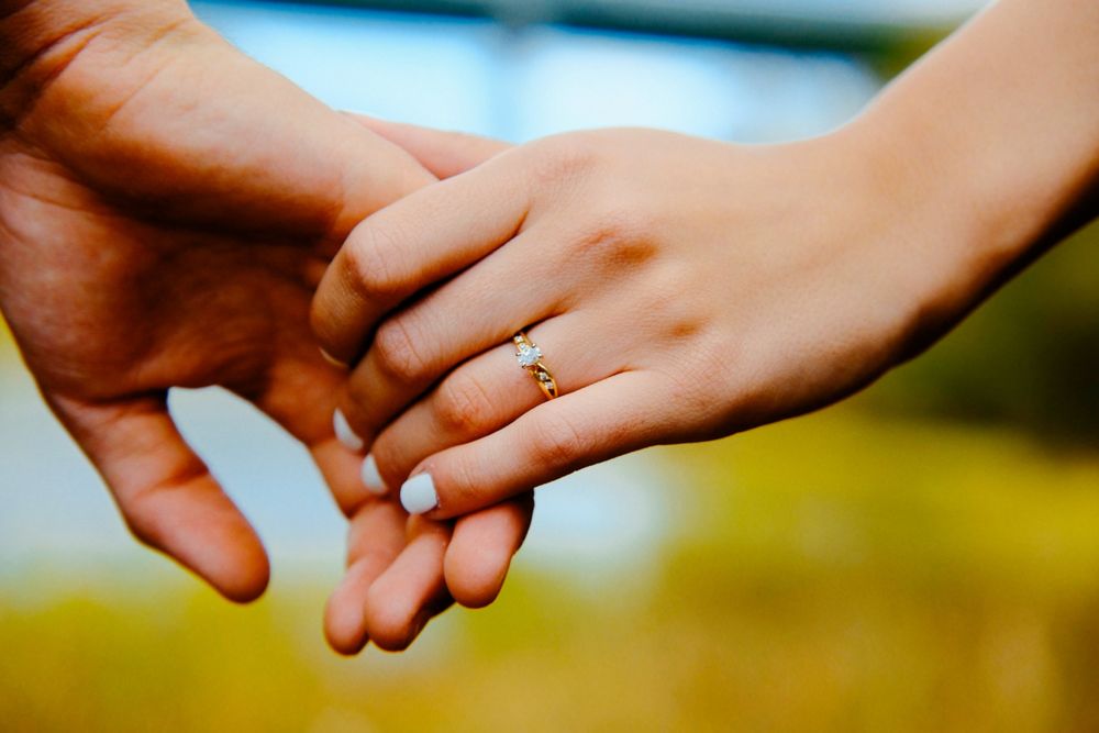 Two hands reach towards each other against a blurred green and yellow background in a tender gesture.