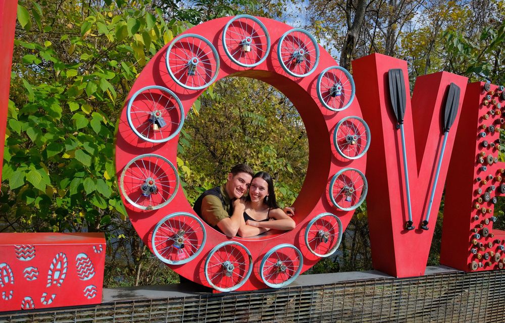 Red love-themed outdoor photo display with circular wreath made of picture frames and decorative letters against greenery.