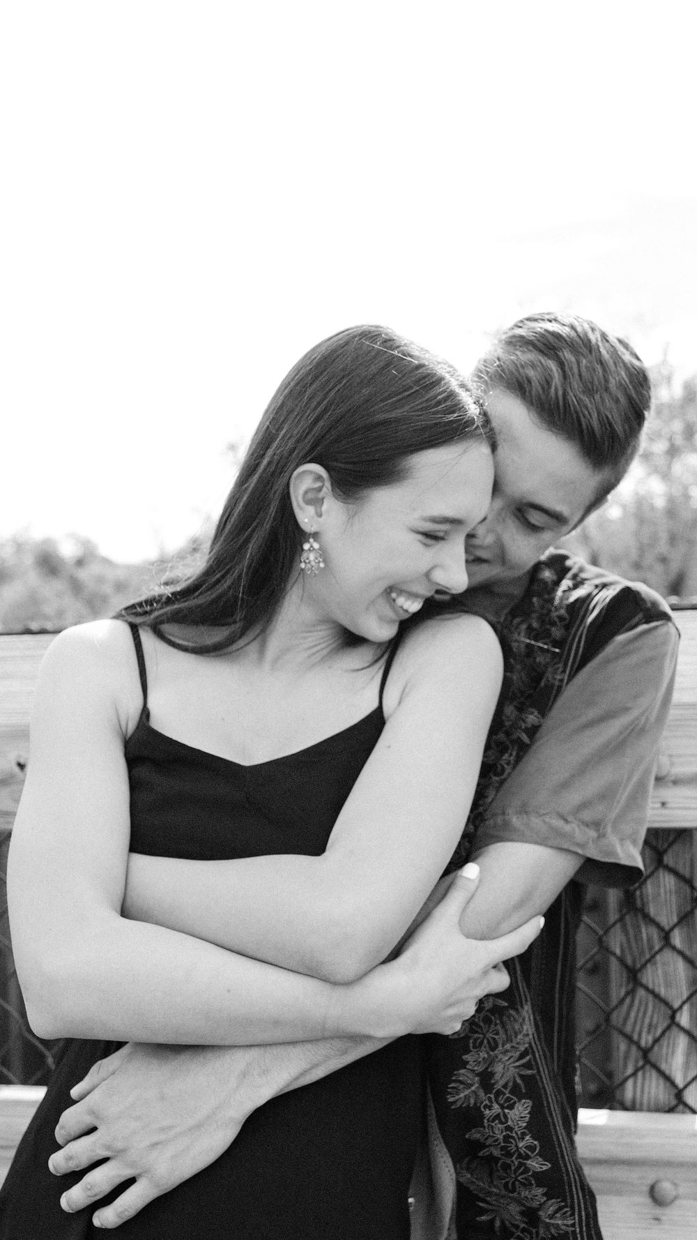 A couple shares an intimate black and white moment together, embracing and laughing on a deck outdoors.
