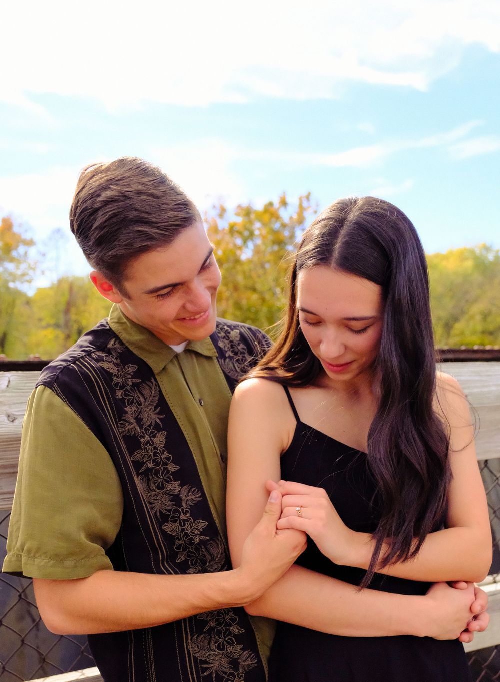 A couple shares a tender moment outdoors during autumn, wearing casual attire as they embrace and smile together.