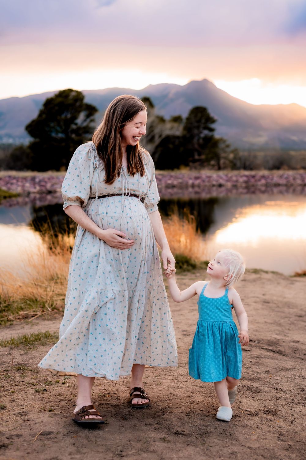 A sunset maternity photoshoot by a serene lake with mountains in the background.