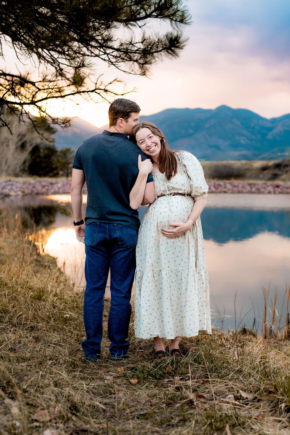 A couple shares a tender moment by a mountain lake during sunset.