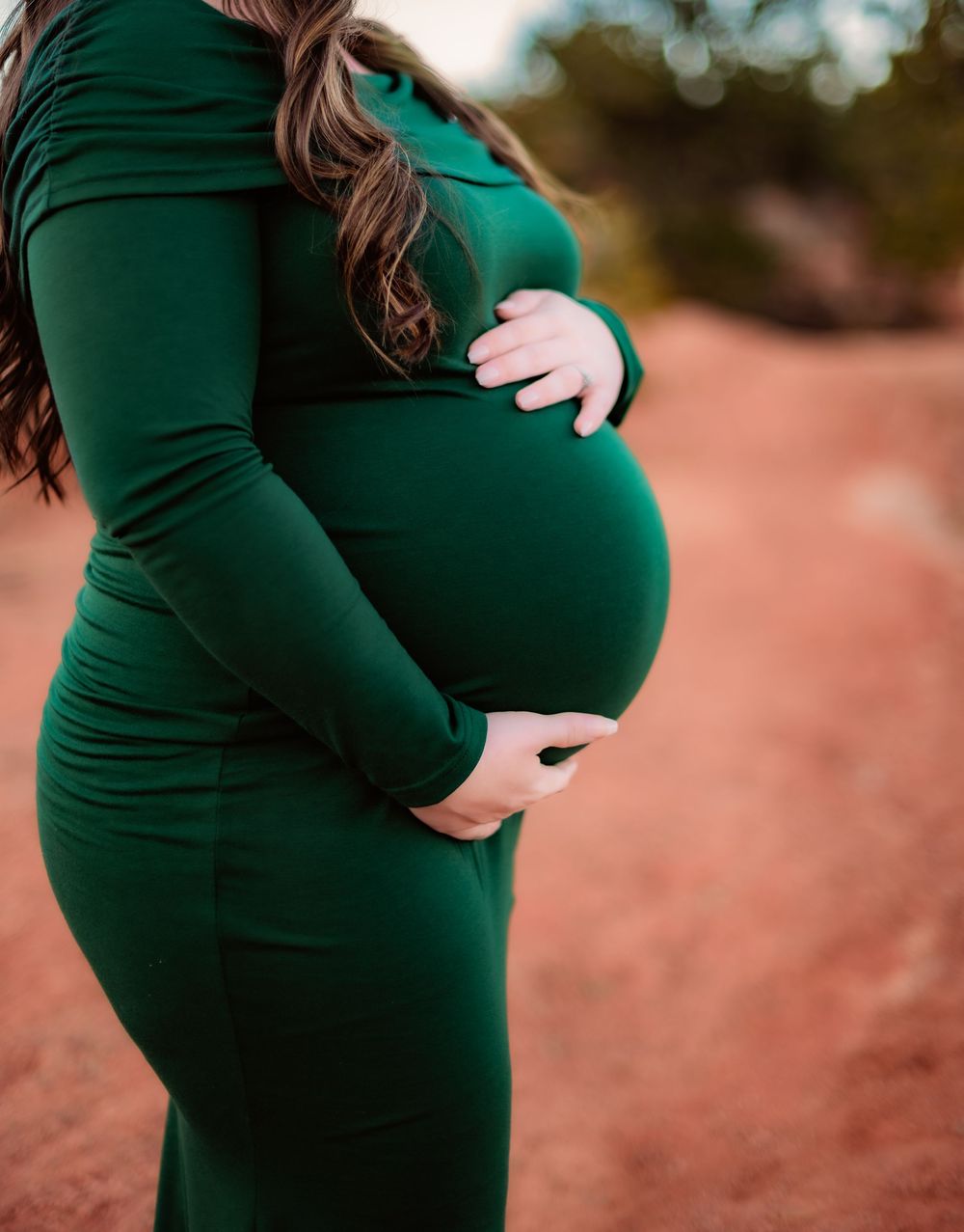 Close-up of a pregnant belly in an emerald green fitted dress against a desert landscape.
