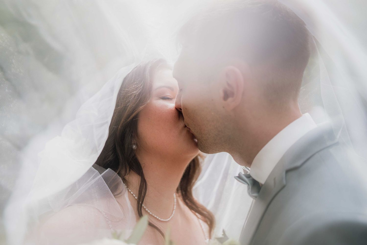 Romantic wedding moment captured through delicate veil with couple sharing a kiss.