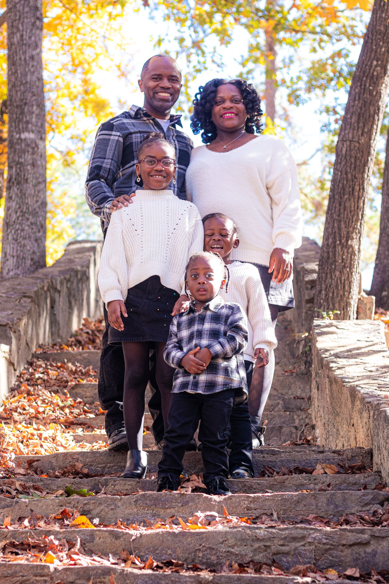 A family of five poses together on stone steps surrounded by fall foliage.
