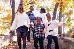 A family plays and jumps together on stone steps during autumn.