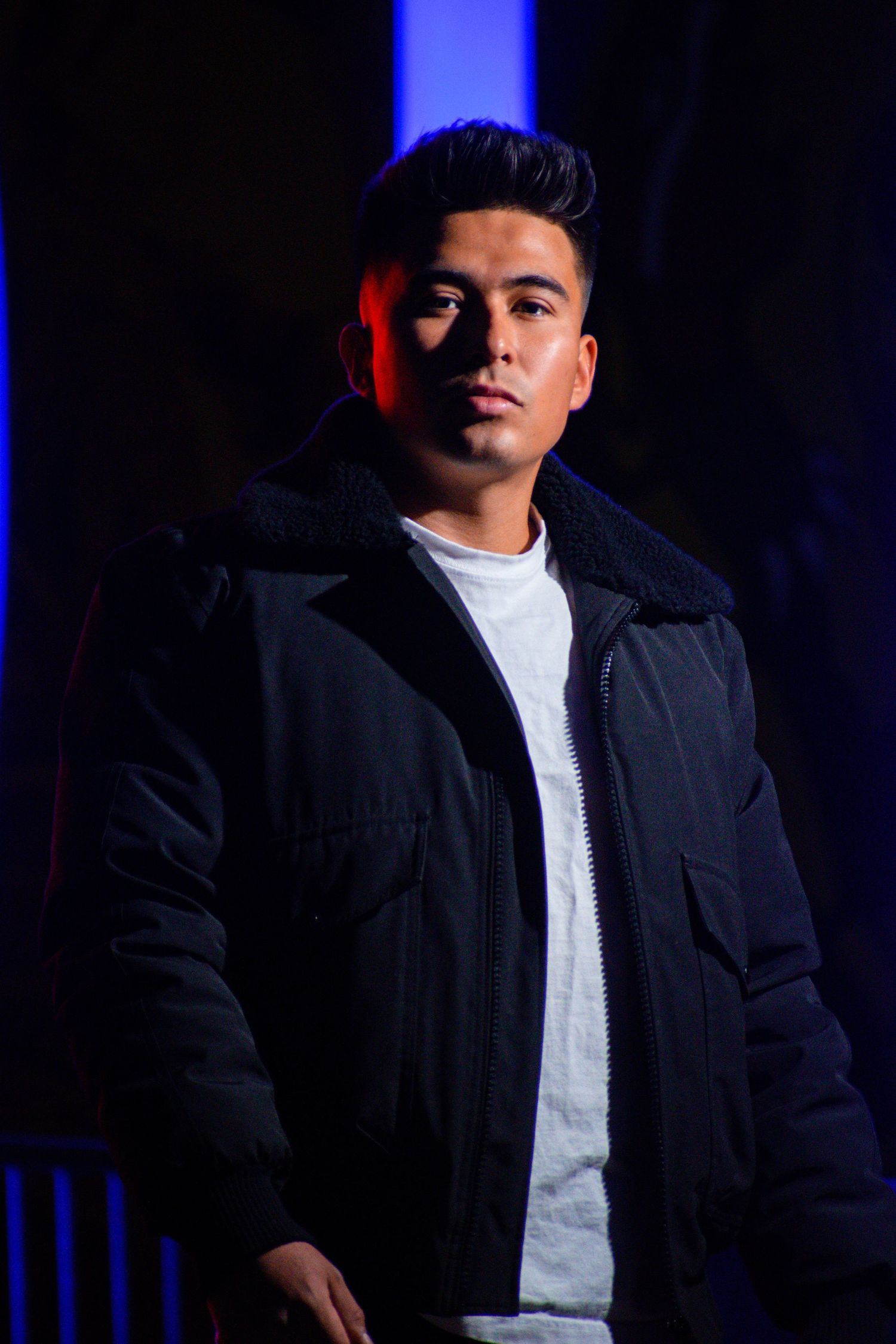 Young man in black puffer jacket posing dramatically under blue and red lighting at night. Toronto GTA