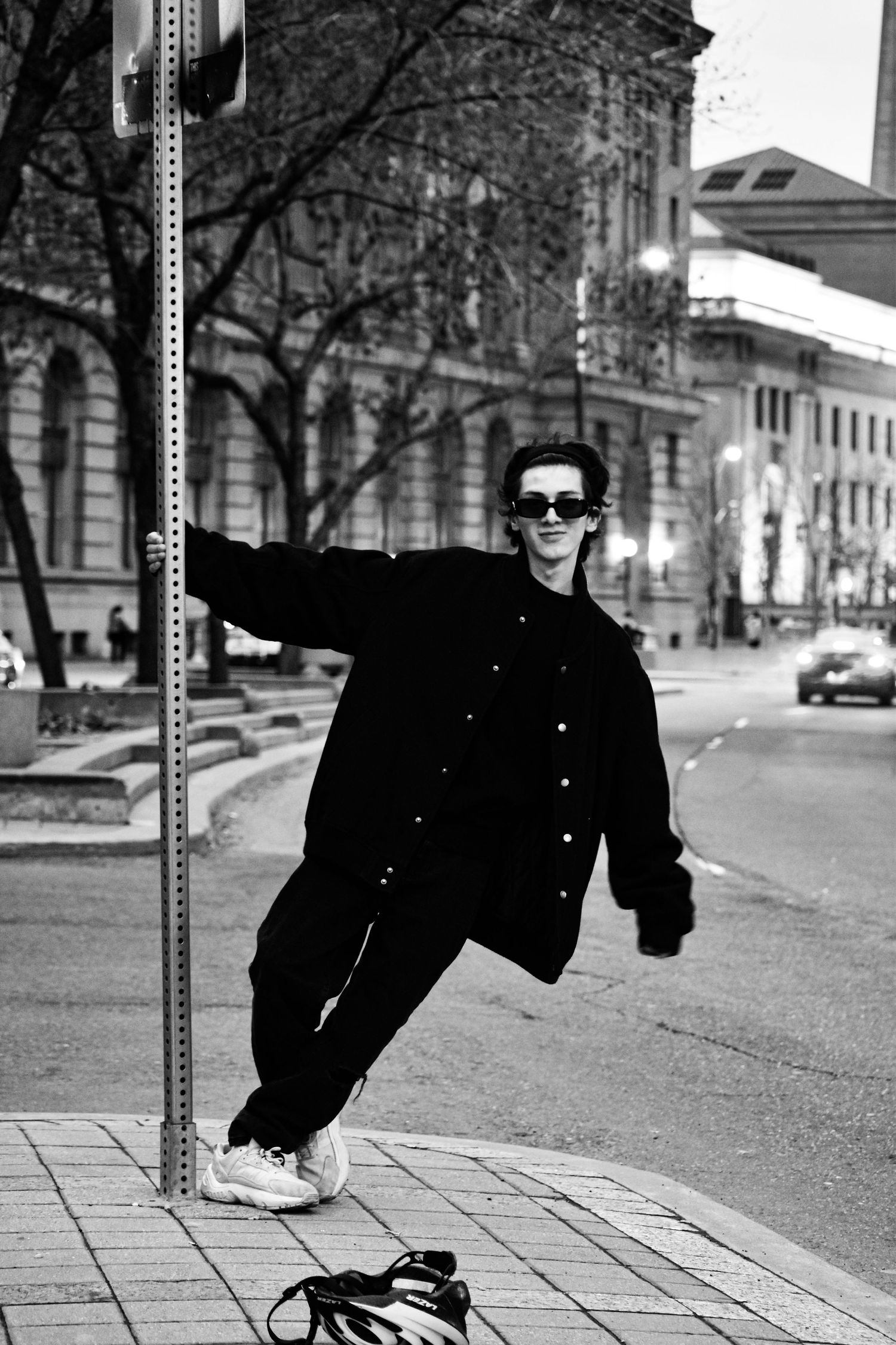 Black and white photo of a young man in sunglasses leaning on a street pole in a city. Toronto GTA