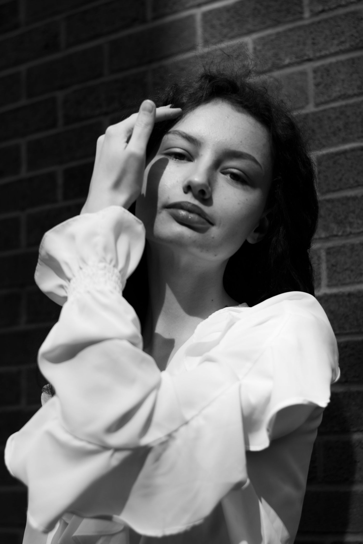 Black and white portrait of a young woman in a white blouse posing against a brick wall. Toronto GTA