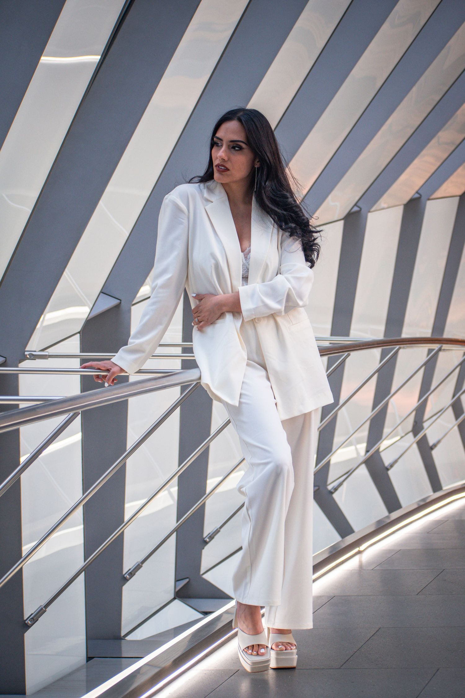 Elegant woman in a white pantsuit posing on a modern architectural staircase with metal railings. Toronto GTA