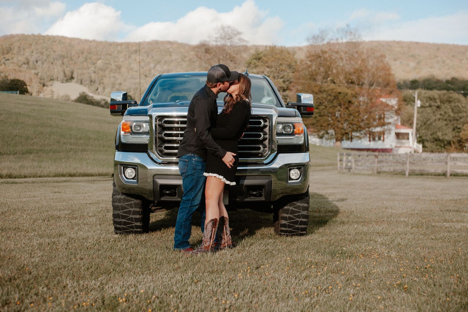 Couple sharing a kiss in front of a lifted GMC truck on a scenic farm property.