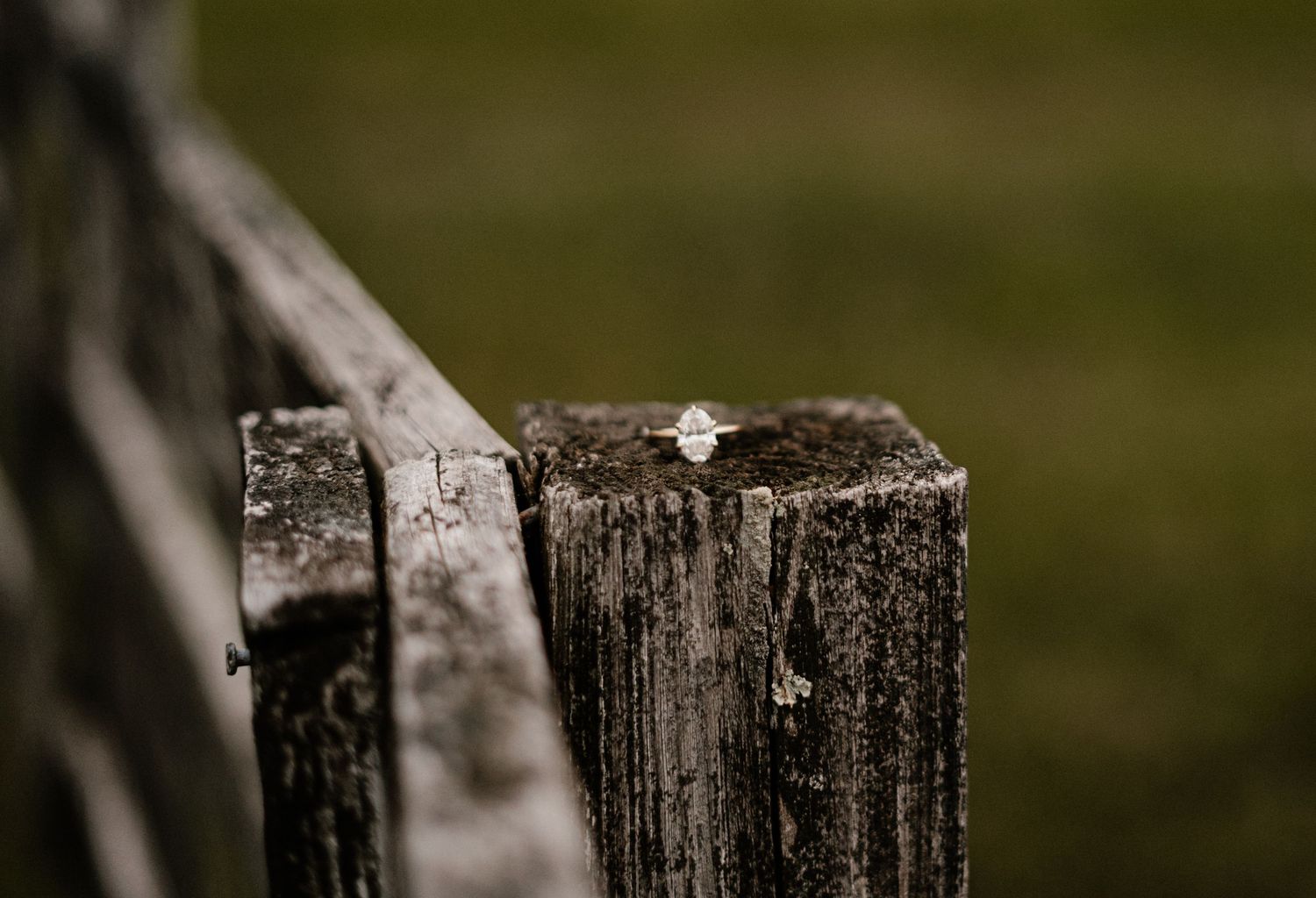 Diamond engagement ring resting on a weathered wooden fence post in a rustic outdoor setting.