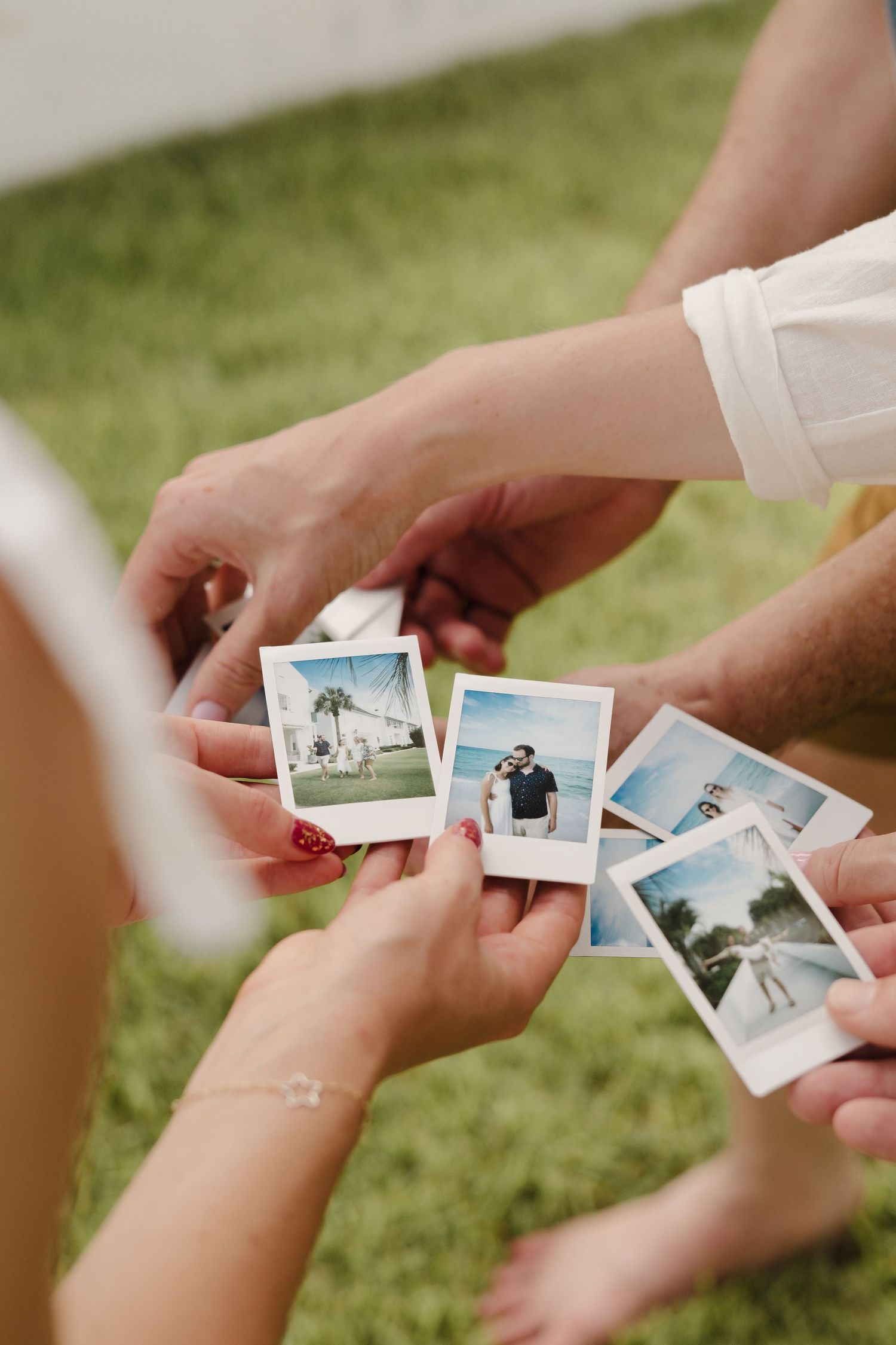 Hands sharing and exchanging polaroid photographs on a grass background.