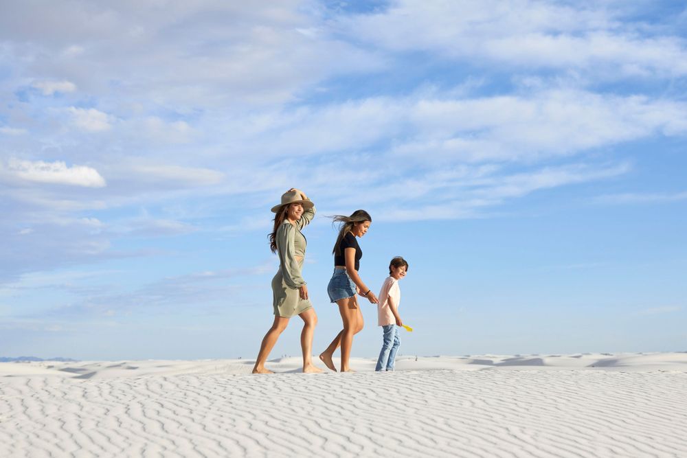 People walking and playing on pristine white sand dunes with mountains in background.