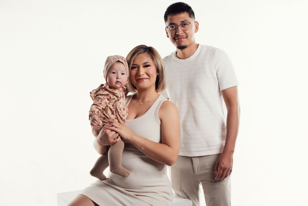 Family posing together in casual white outfits against studio backdrop.