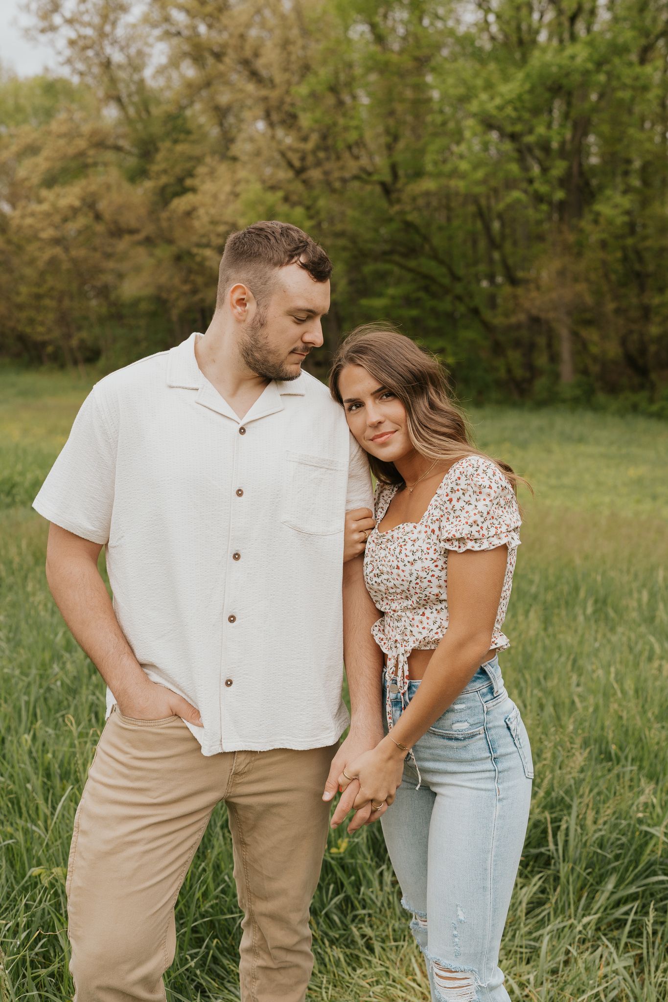 Casual couple in light summer clothing posing playfully together in a tall grass field. Taken in Concord MI