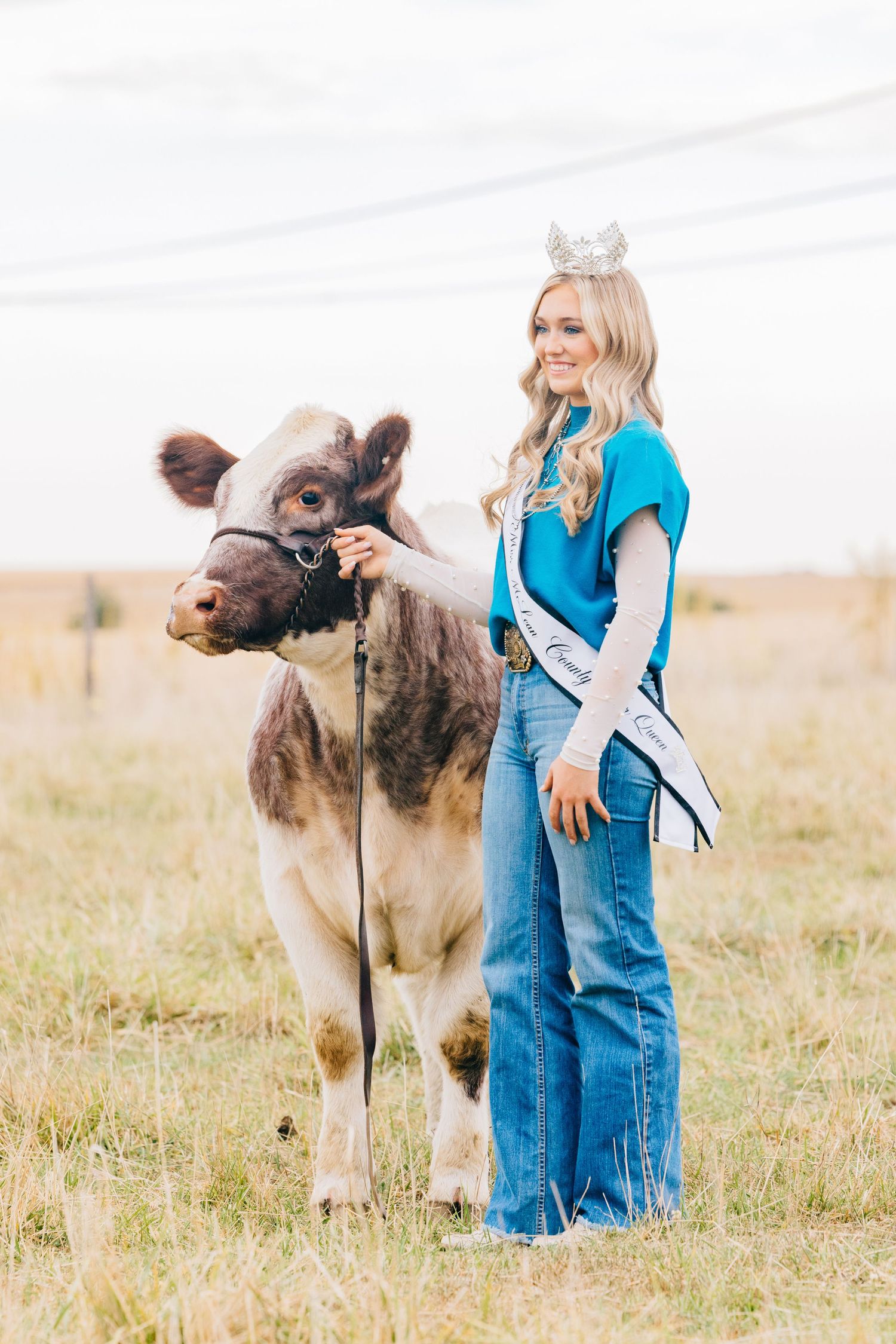 Senior fair queen posing with her show heifer in a field