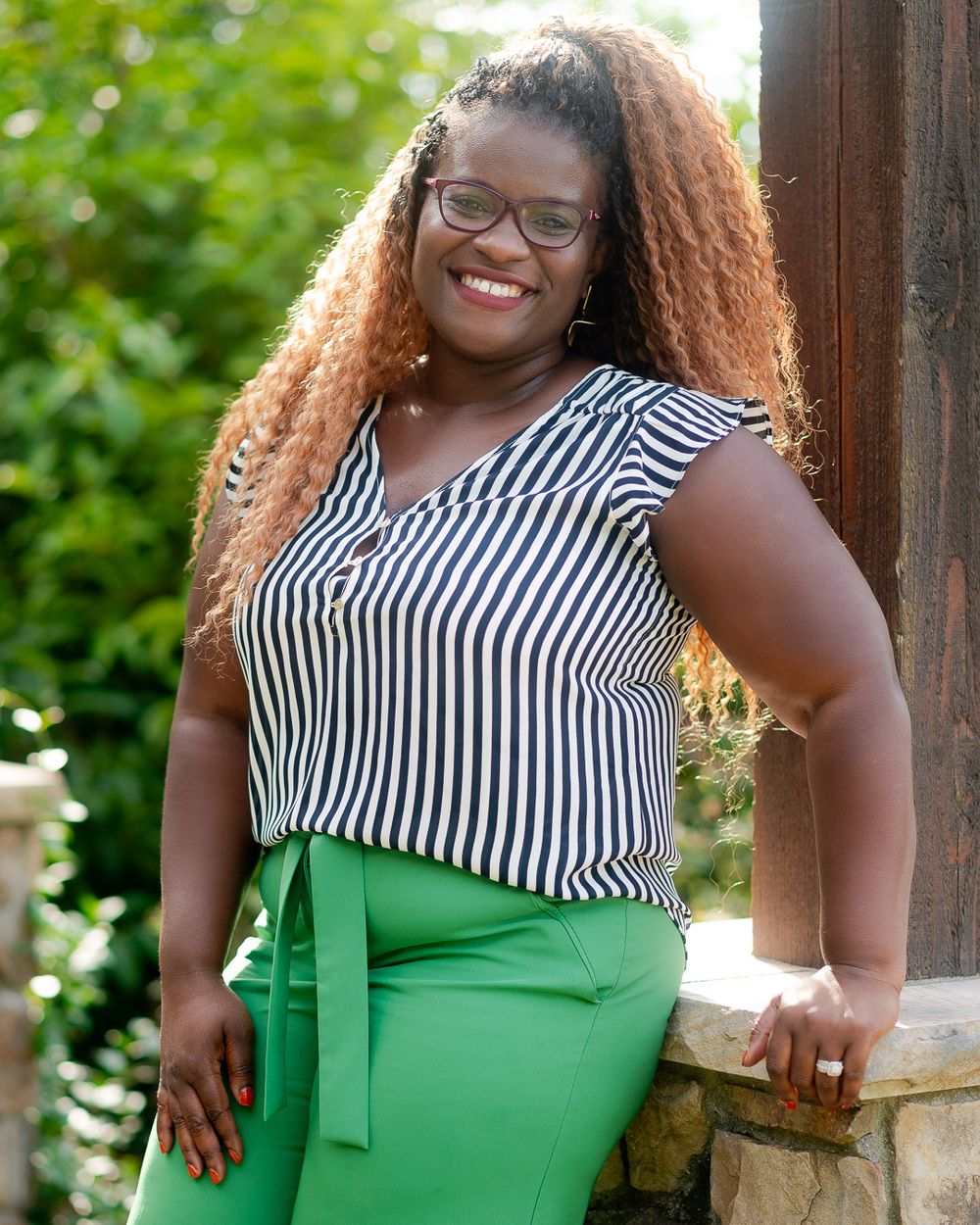Style portrait of person in striped top and green skirt leaning against wooden column outdoors.