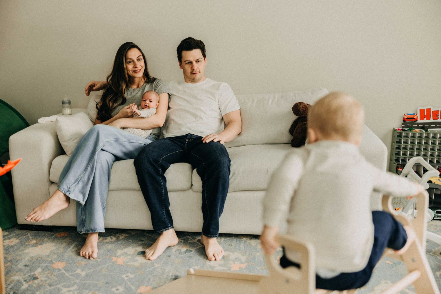Family relaxing together on living room couch while child plays on floor.