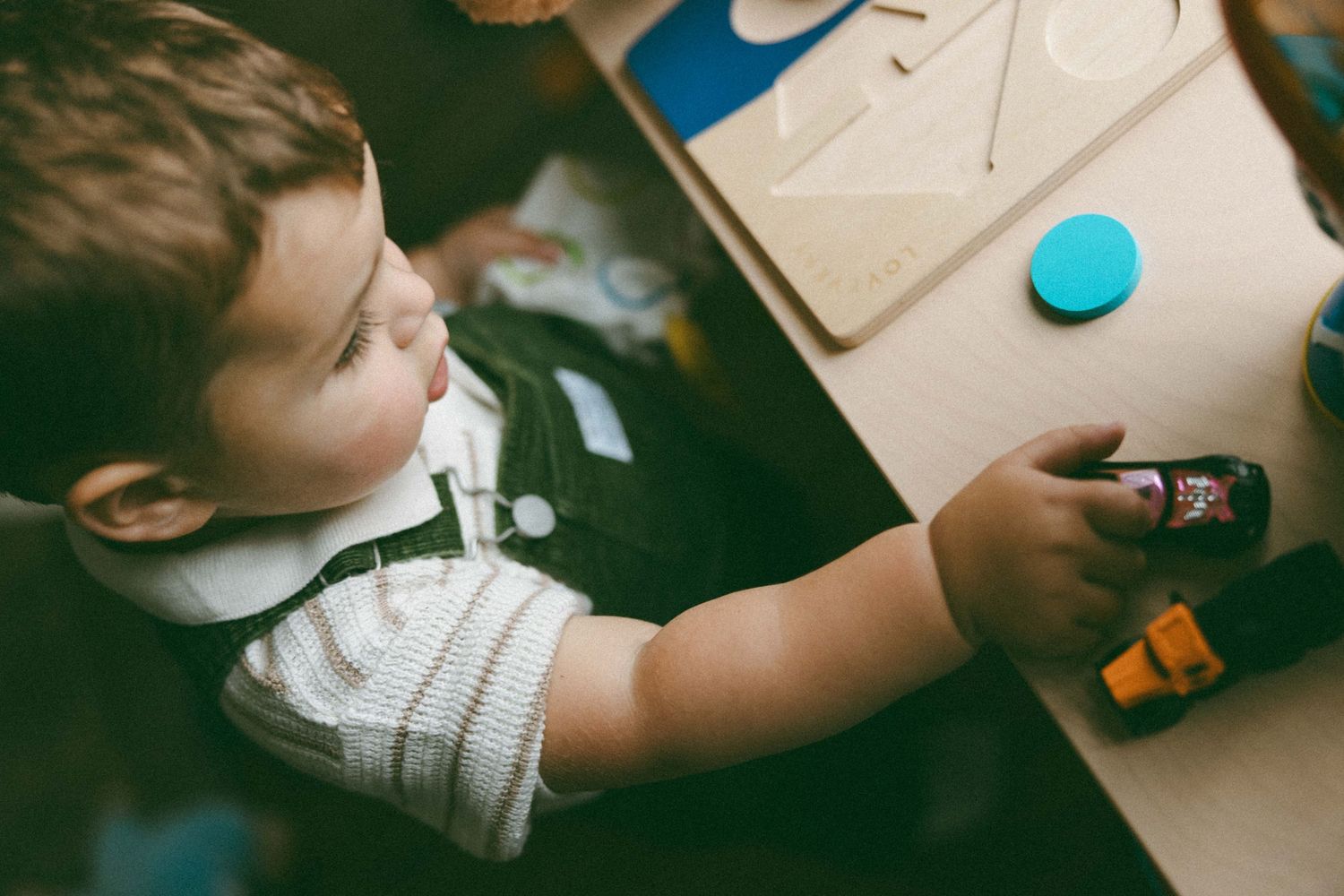 Young toddler boy holding a glue stick while doing a craft activity at a wooden table.