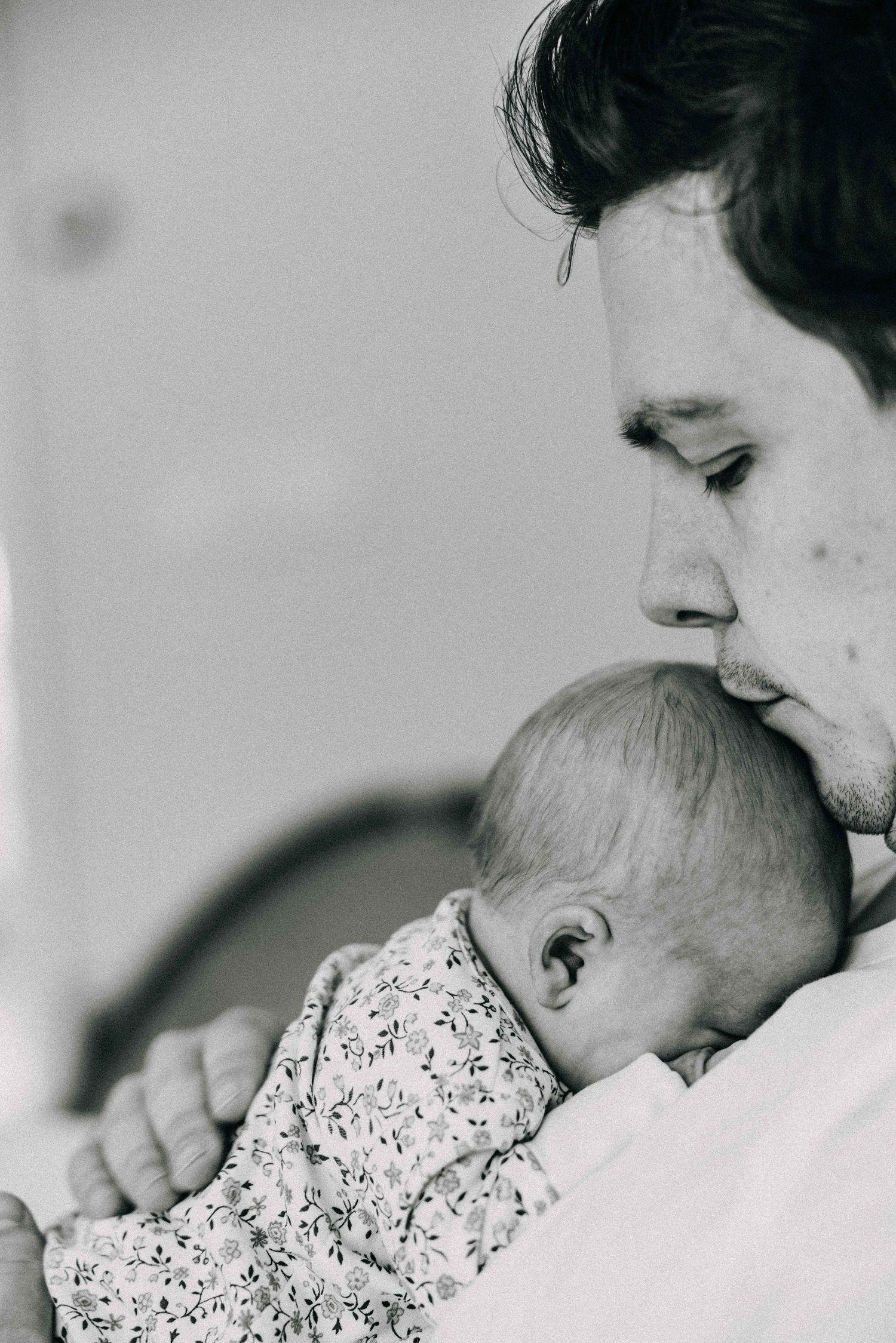 Black and white close-up of a tender moment showing affection to a sleeping baby in floral clothing.