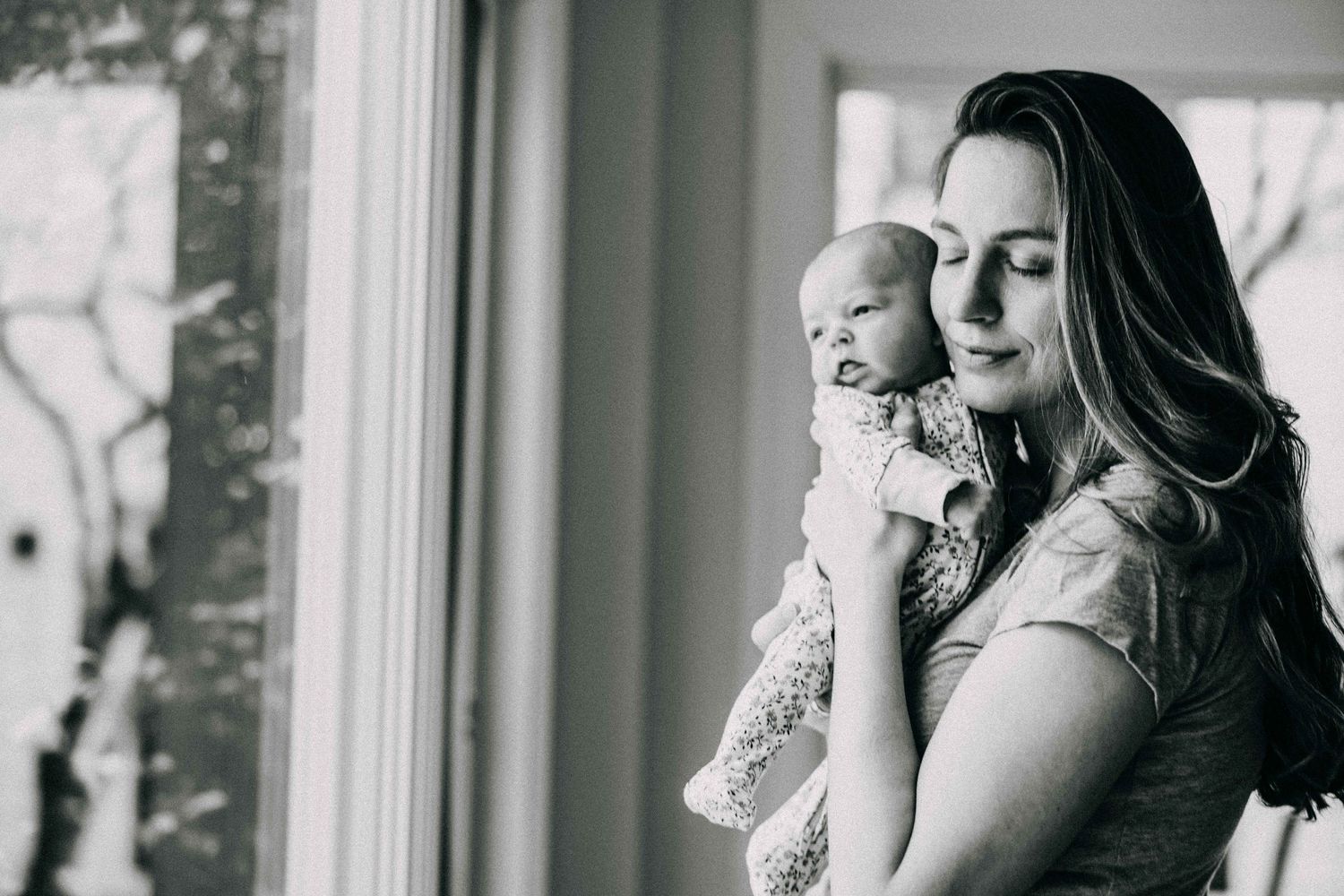 Black and white portrait of tender moment between parent and baby by window.