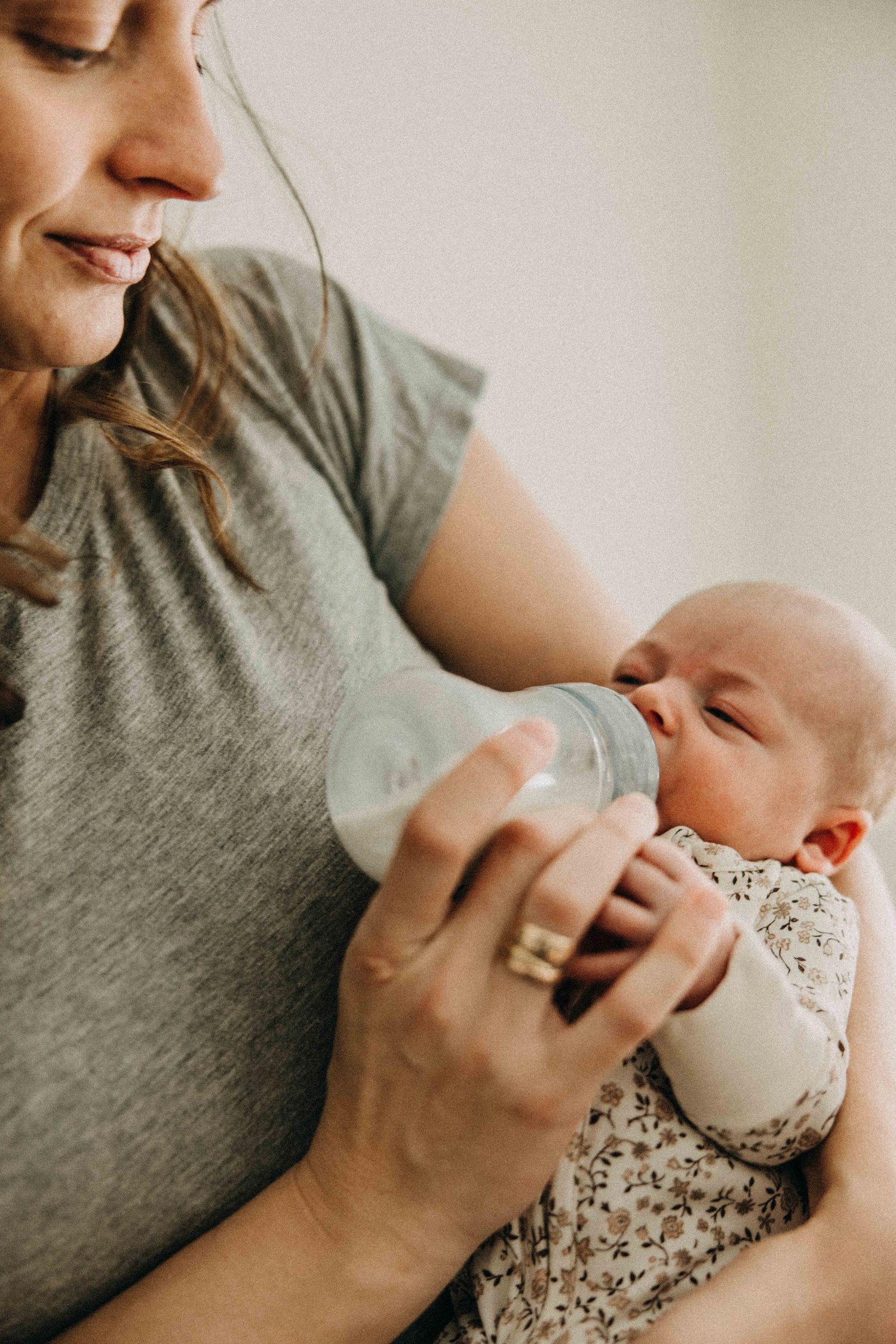 Baby drinking from bottle while being held in grey shirt-clad arms.