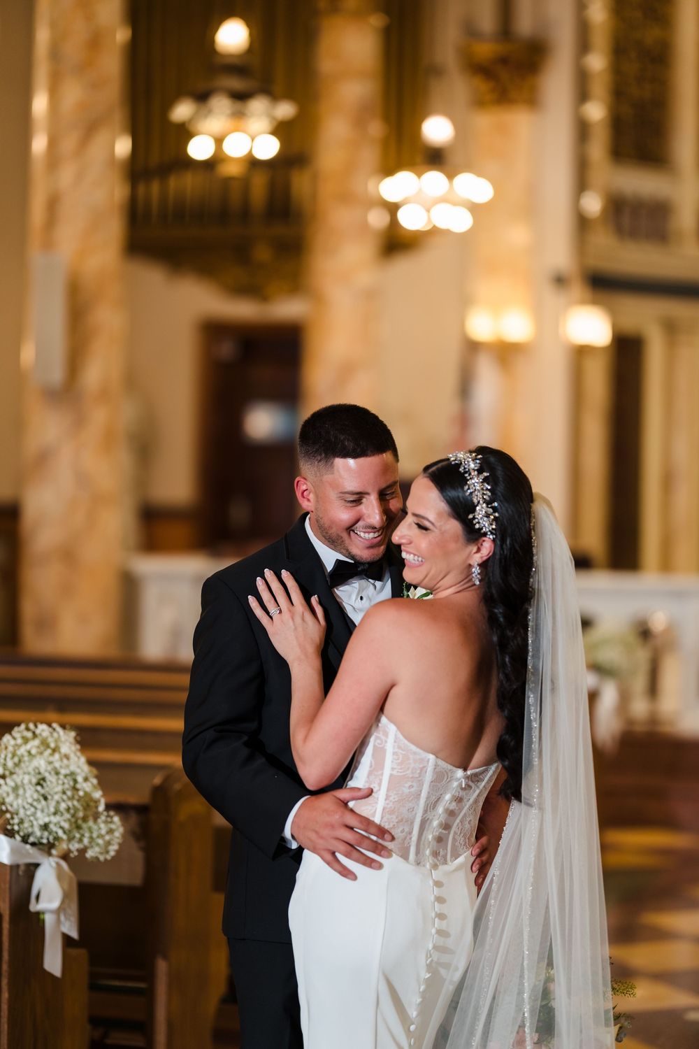 Newlywed couple shares an intimate moment in an elegant church with ornate lighting and floral decorations.