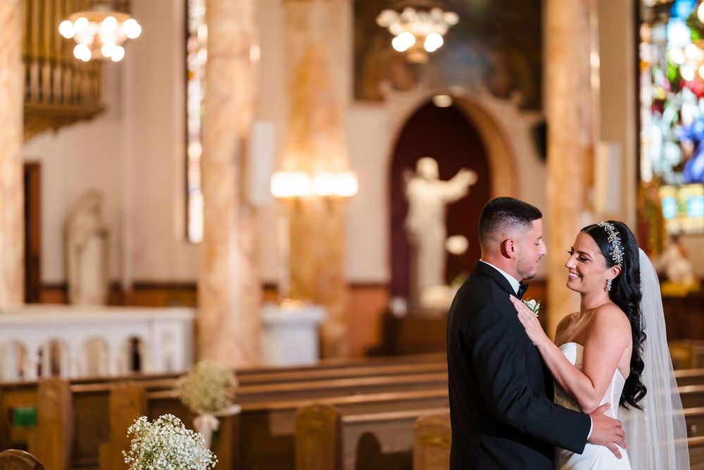 A romantic wedding couple shares a tender kiss in a beautifully lit church sanctuary with stained glass windows.