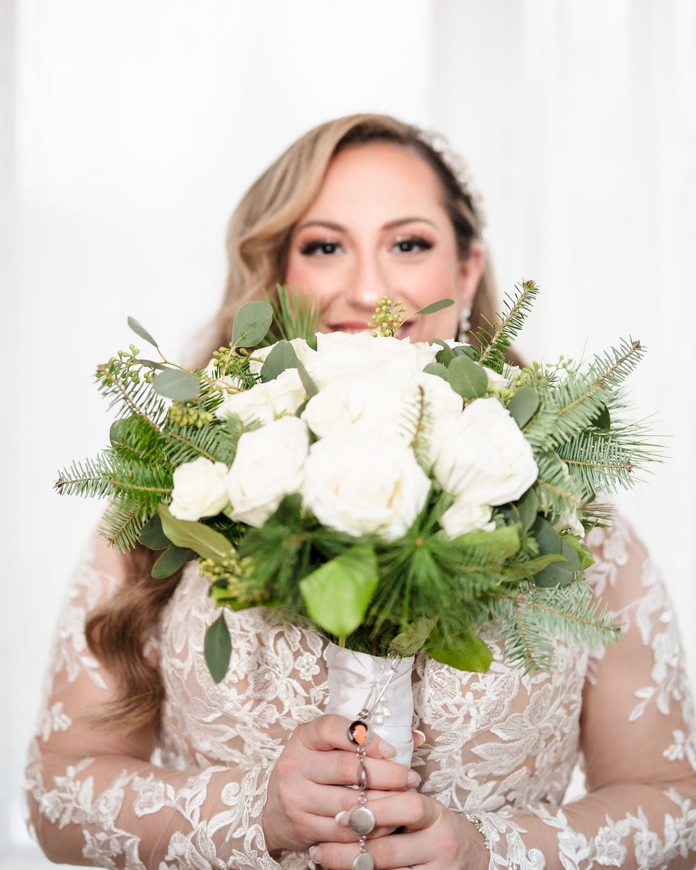 Bride holding winter-inspired bouquet with white roses and evergreen sprigs.