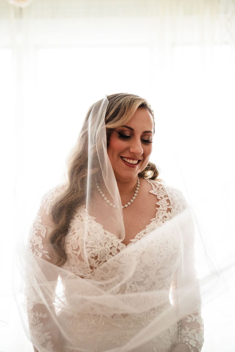 Ethereal bridal portrait with white veil and pearl necklace in natural light.