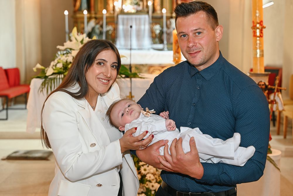 A couple holds their newborn baby during a baptism ceremony in an elegant church setting.